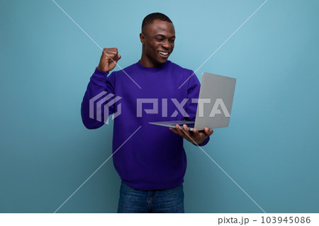 30s dark-skinned American man dressed in a blue sweater works remotely with a laptop 30s dark-skinned American man dressed in a blue sweater works remotely with a laptop 103945086