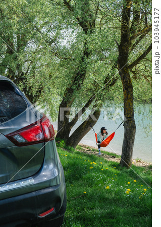 A woman in a cap rests in a hammock overlooking the river A woman in a cap rests in a hammock overlooking the river 103945177