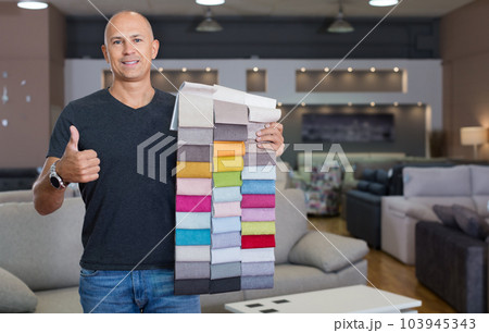 Sales consultant demonstrating samples of upholstery fabric 103945343