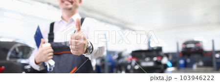 Master repairman holding clipboard with documents and showing thumb to auto repair shop 103946222