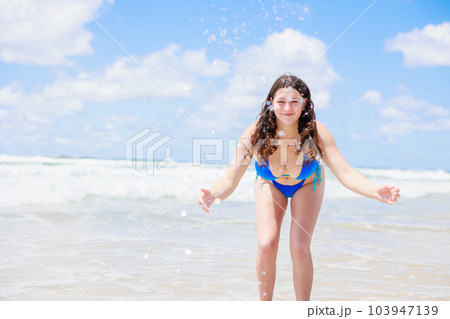 海辺でカメラに向かって水をかける水着のセクシーな女の子 103947139