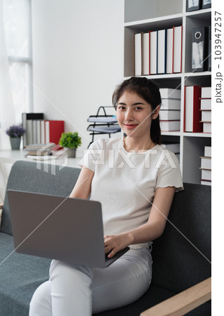 Young relaxed smiling pretty woman relaxing sitting on sofa at home. Female feeling joy enjoying with laptop on cozy couch 103947257