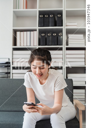 Young relaxed smiling pretty woman relaxing sitting on sofa at home. Female feeling joy enjoying with mobile phone on cozy couch Young relaxed smiling pretty woman relaxing sitting on sofa at home. Female feeling joy enjoying with mobile phone on cozy couch 103947346