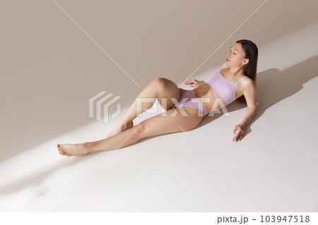 Top view young girl with fit, slim figure lying on floor, posing in underwear against grey studio background. Tenderness Top view young girl with fit, slim figure lying on floor, posing in underwear against grey studio background. Tenderness 103947518