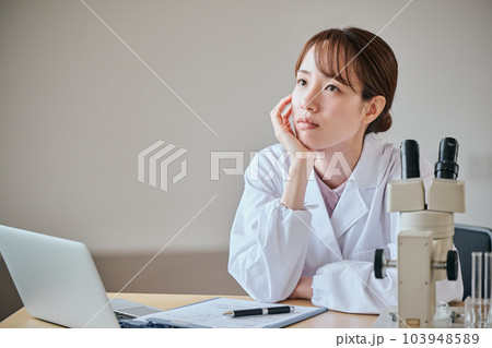 頬杖をついて考え事をする白衣の若い女性 103948589