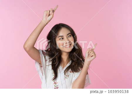 Young Asian woman pointing fingers up to empty space isolated pink color background Young Asian woman pointing fingers up to empty space isolated pink color background 103950138