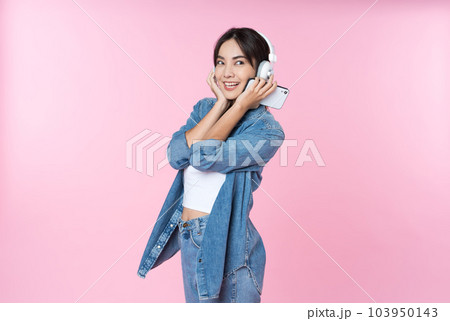 Young Asian woman wearing headphones dancing and listening to music from smartphone shoot in isolated on pink background 103950143