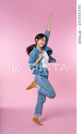 Young Asian woman wearing headphones dancing and listening to music from smartphone shoot in isolated on pink background Young Asian woman wearing headphones dancing and listening to music from smartphone shoot in isolated on pink background 103950145