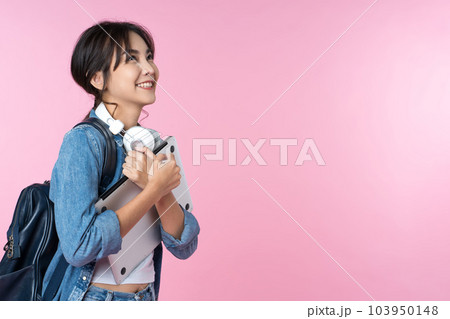 Portrait of smiling young Asian college student look to the side of the empty space with laptop and backpack isolated over pink background 103950148