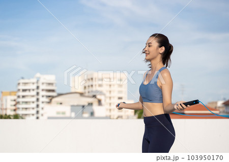 Young Asian woman with jump rope on rooftop. Fitness female doing skipping workout outdoors 103950170
