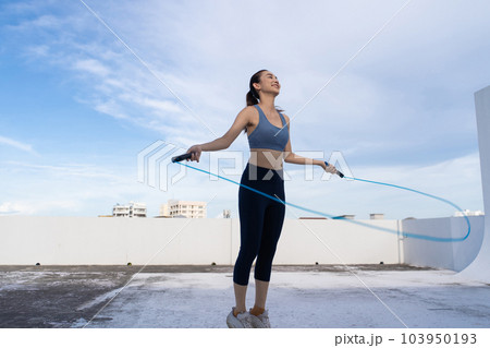 Young Asian woman with jump rope on rooftop. Fitness female doing skipping workout outdoors 103950193