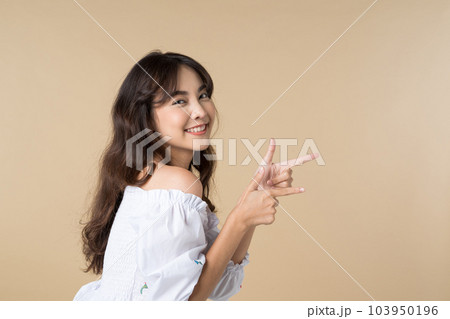 Young Asian woman pointing fingers up to empty space isolated brown color background 103950196