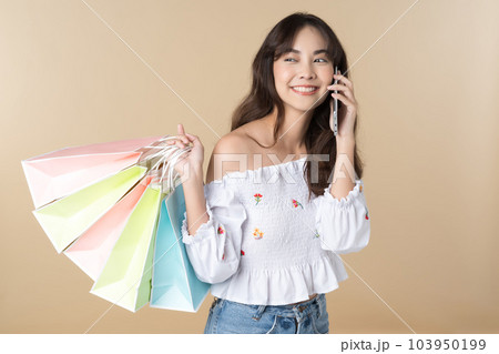Young Asian woman usin shopping bag using phone on isolate brown background 103950199