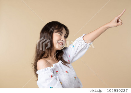 Young smiling Asian woman pointing finger sideways to copy space in brown color background. Young smiling Asian woman pointing finger sideways to copy space in brown color background. 103950227