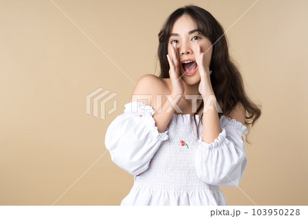 Young Asian woman doing a shocked surprise gesture shouting with hands cupped around mouth isolated brown color background 103950228
