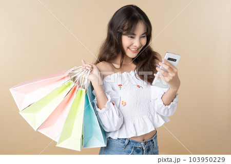 Young Asian woman carrying colorful bags shopping online with mobile phone isolate brown background. 103950229