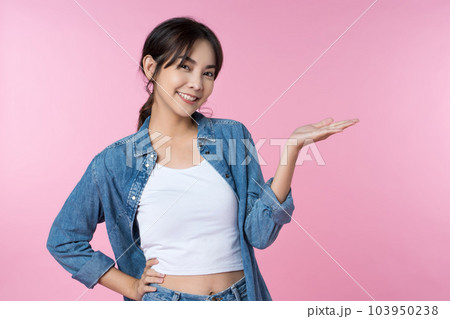 Young happy Asian woman pointing showing hands up presentation to copy space she wearing jean shoot in isolated on pink background Young happy Asian woman pointing showing hands up presentation to copy space she wearing jean shoot in isolated on pink background 103950238