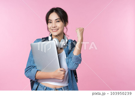 Portrait of smiling young Asian college student with laptop and backpack isolated over pink background.Cheer up success celebration concept Portrait of smiling young Asian college student with laptop and backpack isolated over pink background.Cheer up success celebration concept 103950239