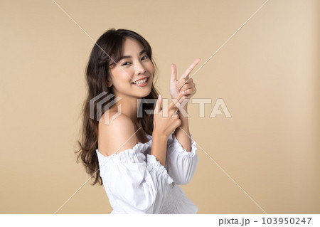 Young Asian woman pointing fingers up to empty space isolated brown color background 103950247