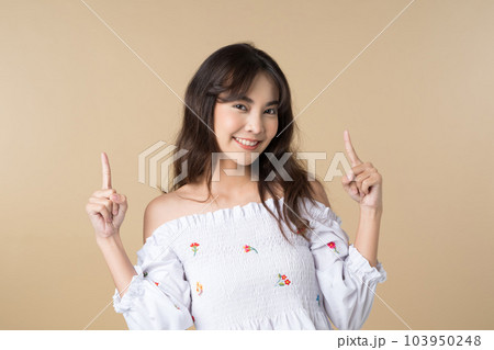 Young Asian woman pointing fingers up to empty space isolated brown color background Young Asian woman pointing fingers up to empty space isolated brown color background 103950248