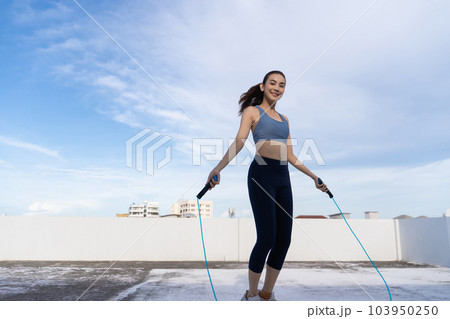 Young Asian woman with jump rope on rooftop. Fitness female doing skipping workout outdoors 103950250