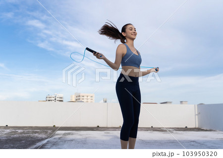 Young Asian woman with jump rope on rooftop. Fitness female doing skipping workout outdoors Young Asian woman with jump rope on rooftop. Fitness female doing skipping workout outdoors 103950320
