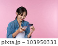 Young beauty Asian woman shopping payment online with credit card on smartphone and she wearing jean and looking at phone isolated on pink background 103950331