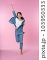Elegant young Asian woman raises her arm and leg in a studio shot, expressing happiness and success isolated pink background 103950333