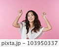 Young Asian woman pointing fingers to empty space isolated pink color background 103950337
