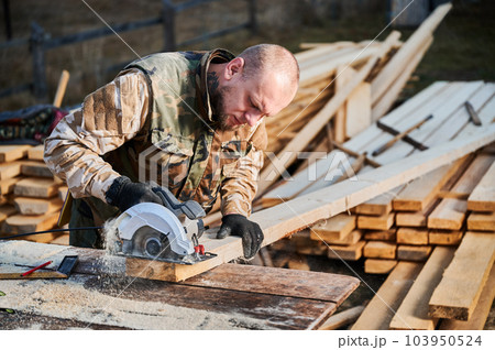 Carpenter using circular saw for cutting wood beam. Man worker building wooden frame house. Carpentry concept. Carpenter using circular saw for cutting wood beam. Man worker building wooden frame house. Carpentry concept. 103950524