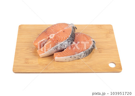 Two salmon steaks on a wooden cutting board over a white background. Two salmon steaks on a wooden cutting board over a white background. 103951720