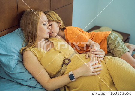Young pregnant mother hugging her little boy lying in bed at night. Caring and loving parent hugging child 103953050