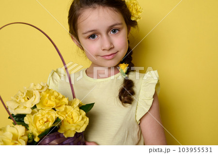 Close-up beauty portrait of a beautiful Caucasian blue eyed little kid girl in yellow dress and flowers in hairstyle, holding a basket with flower, smiling, looking at camera, isolated on background Close-up beauty portrait of a beautiful Caucasian blue eyed little kid girl in yellow dress and flowers in hairstyle, holding a basket with flower, smiling, looking at camera, isolated on background 103955531
