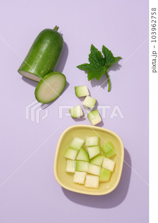 Against a purple background, transparent water with winter melon slices contained inside a bowl. Vitamin C in Winter melon (Benincasa hispida) also exhibits skin brightening effects 103962758