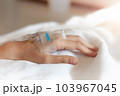 Closeup woman Hand of a patient with medical drip or IV drip lying on bed in hospital, Patient with drip receiving a saline solution. free space for text 103967045