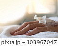 Closeup woman Hand of a patient with medical drip or IV drip lying on bed in hospital, Patient with drip receiving a saline solution. free space for text 103967047