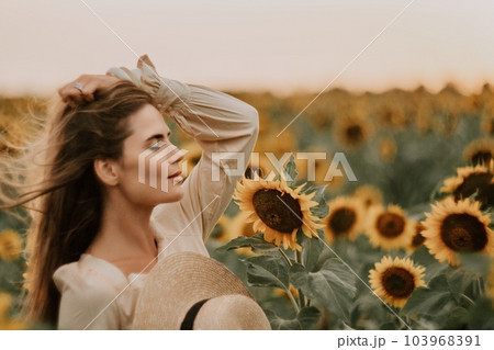 Woman in Sunflower Field: Happy girl in a straw hat posing in a vast field of sunflowers at sunset, enjoy taking picture outdoors for memories. Summer time. 103968391