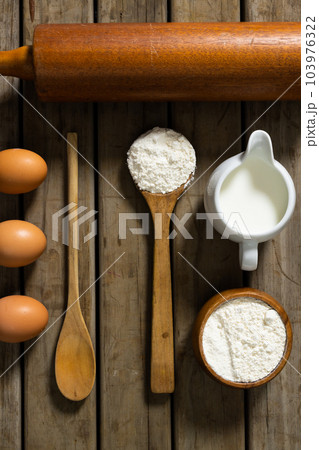 Directly above shot of flour, sugar, milk, eggs with wooden spoons and rolling pin on table 103976322