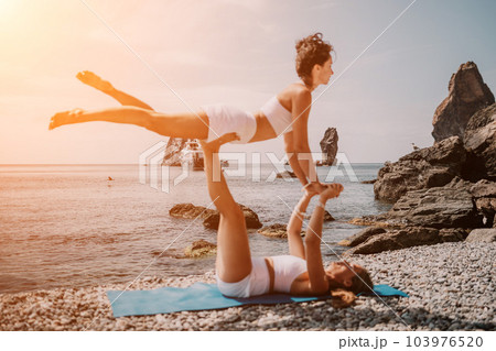 Woman sea yoga. Two happy women practicing yoga on the beach with ocean and rock mountains. Motivation and inspirational fit and exercising. Healthy lifestyle outdoors in nature, fitness concept. 103976520