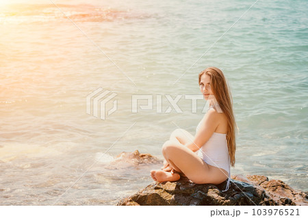 Woman summer travel sea. Happy tourist enjoy taking picture outdoors for memories. Woman traveler posing on the beach at sea surrounded by volcanic mountains, sharing travel adventure journey 103976521