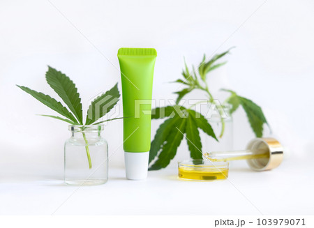 Cream tube and pipette with CBD oil near green cannabis leaves closeup on white, Cosmetic mockup 103979071