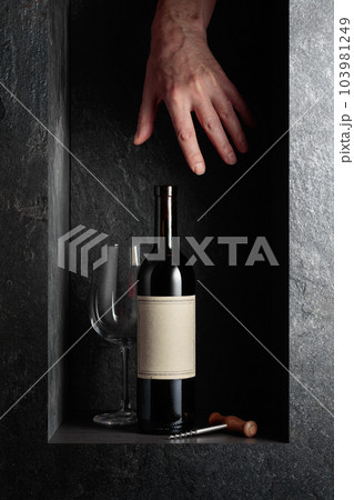 HHand reach for a bottle of red wine with an old empty label. HHand reach for a bottle of red wine with an old empty label. 103981249