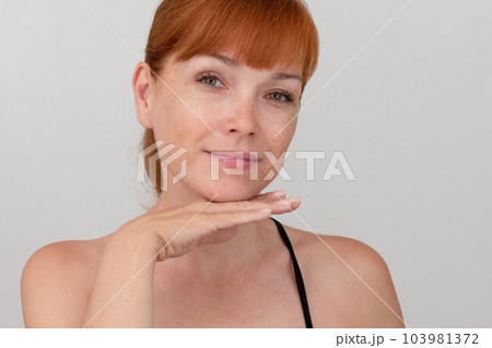 Portrait of cropped caucasian middle aged woman with freckles holding hand under chin on white background looking at camera Portrait of cropped caucasian middle aged woman with freckles holding hand under chin on white background looking at camera 103981372