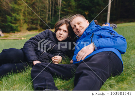 Father laying on his back in the grass with her young daughter. Parenthood and childhood family concept outdoors in nature. happy father and little girl on the grass. Devoted father and daughter lying 103981545