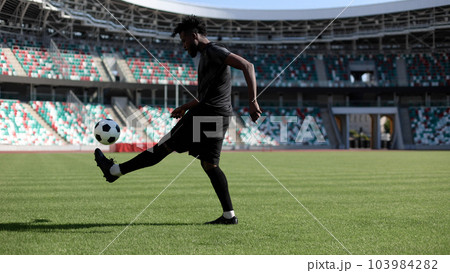 African American man playing football on the stadium field. A man runs with a soccer ball across the field. African American man playing football on the stadium field. A man runs with a soccer ball across the field. 103984282