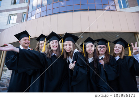 Happy students in graduate gown stand in a row against the backdrop of the university. Happy students in graduate gown stand in a row against the backdrop of the university. 103986173