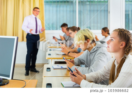 Teenage students using smartphones during lesson 103986682