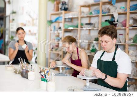 Teenager boy in apron modeling clay pottery in workshop Teenager boy in apron modeling clay pottery in workshop 103986957