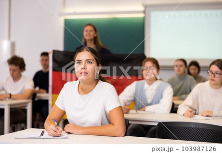 High school teacher holds the flag of Germany in her hands and talks about this country in geography lesson High school teacher holds the flag of Germany in her hands and talks about this country in geography lesson 103987126
