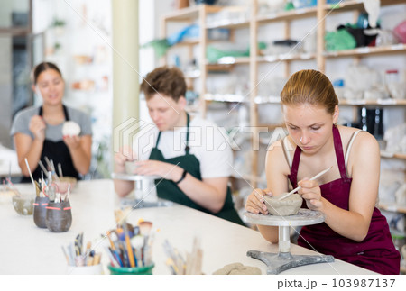 Teenage girl attentively learns how to make pottery with a wooden sticker in workshop 103987137